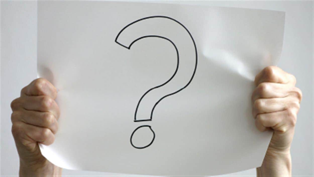 Photo en couleur de mains tenant une feuille sur laquelle est dessiné un point d'interrogation.