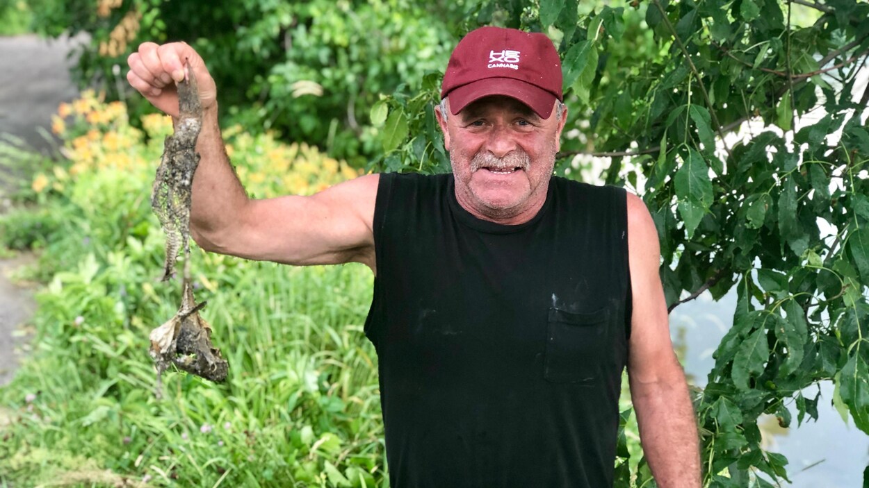 Un homme tient un poisson mort du bout de ses doigts.