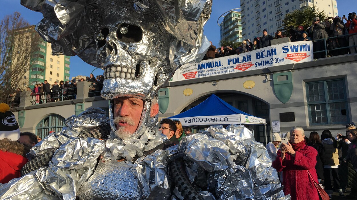 Homme dans un déguisement de couleur argent devant une banderole où il est inscrit Annual Polar Bear Swim. Homme dans un déguisement de couleur argent devant une banderole où il est inscrit Annual Polar Bear Swim.