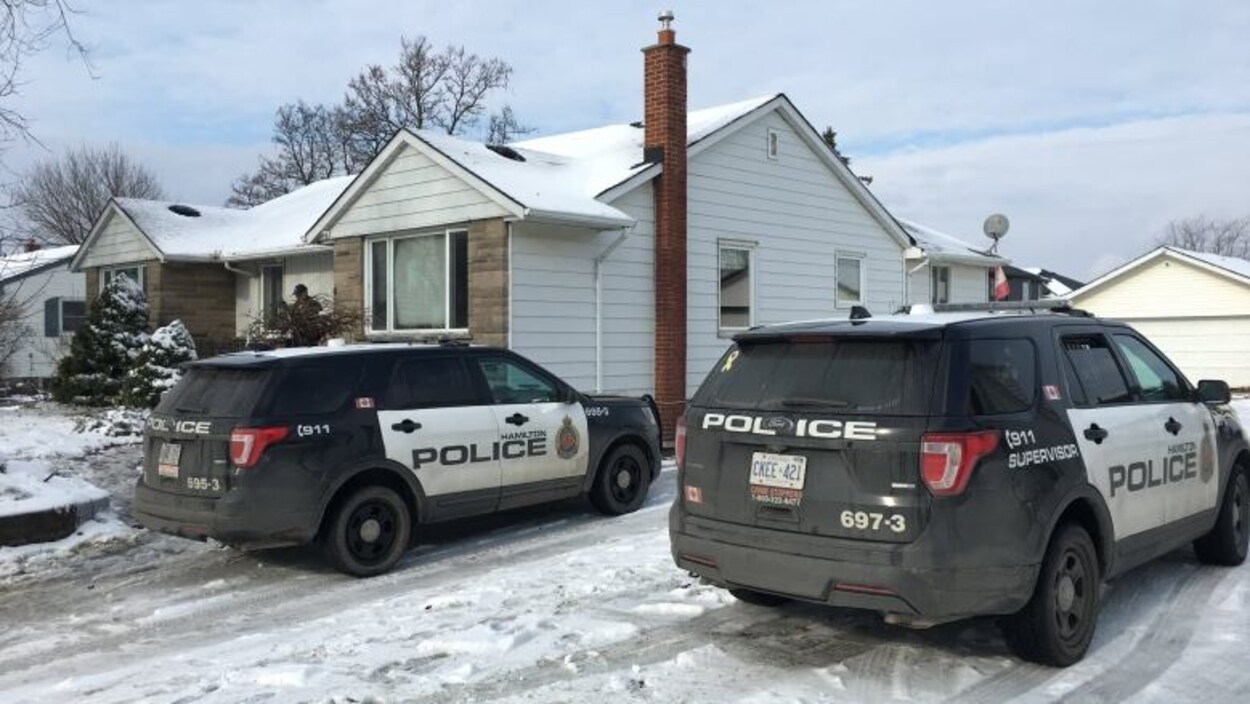 Deux voitures de police devant une maison en hiver.