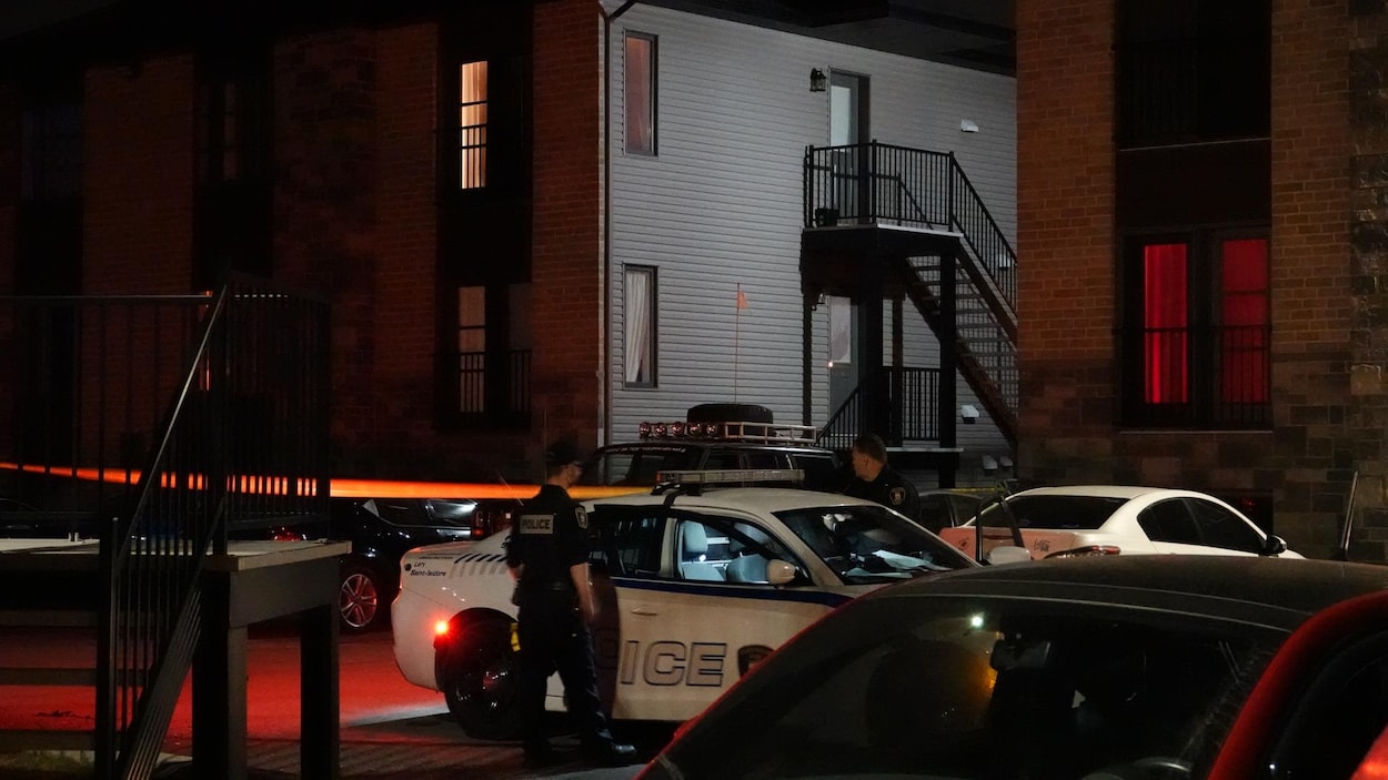Des policiers se tiennent à côté de leur véhicule, stationné près d'un immeuble à logement.