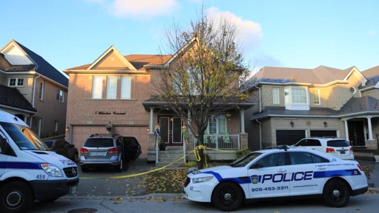 Des voitures de police devant une maison avec un ruban jaune devant une résidence.