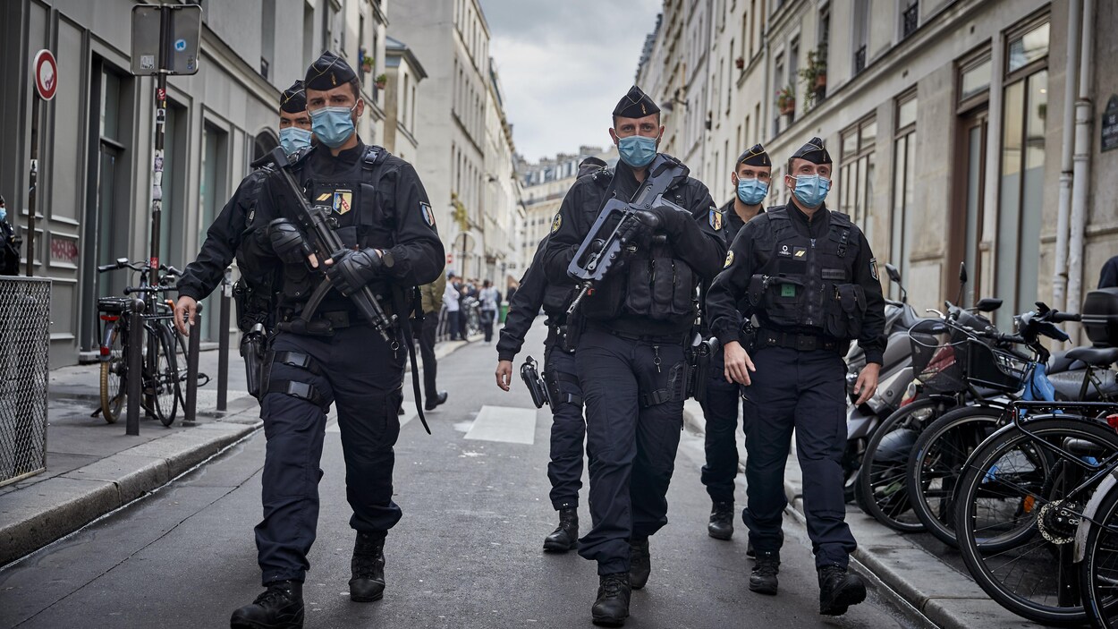 Des agents de police armés de fusils automatiques marchent dans la rue.