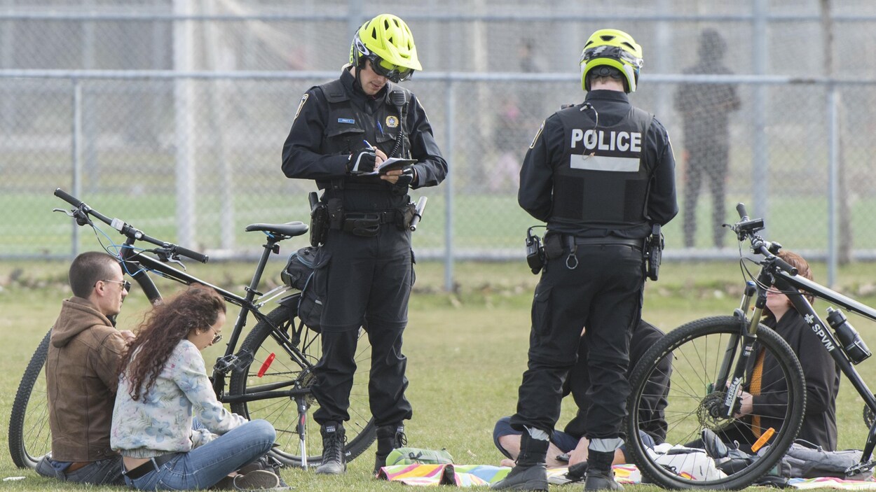 Deux policiers écrivent des contraventions alors que des gens sont assis par terre.