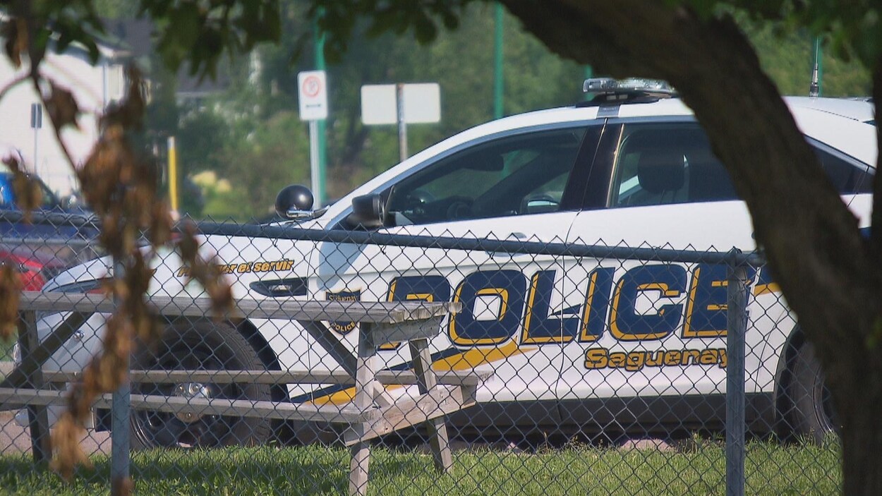 Une voiture de la police de Saguenay est stationnée derrière une clôture.