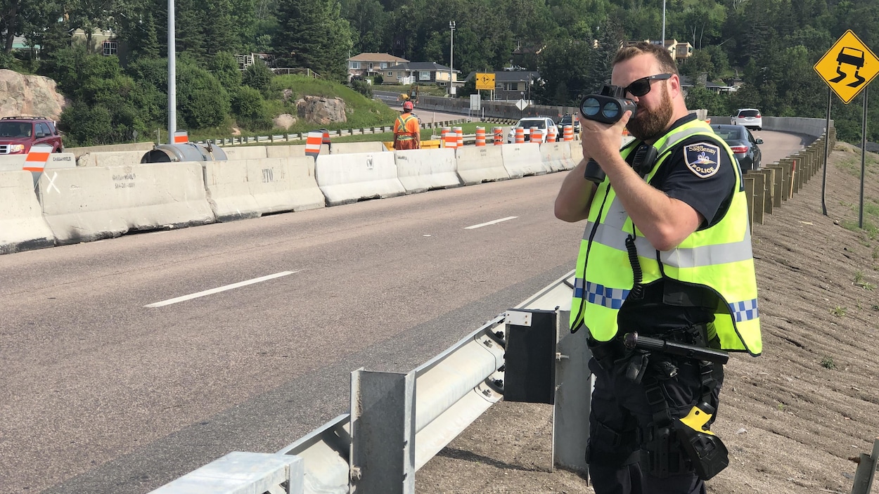 Un policier regarde dans un radar pour détecter la vitesse des automobilistes.
