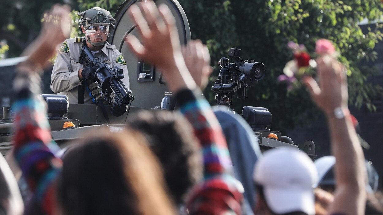 Un policier tient une arme face à des manifestants.