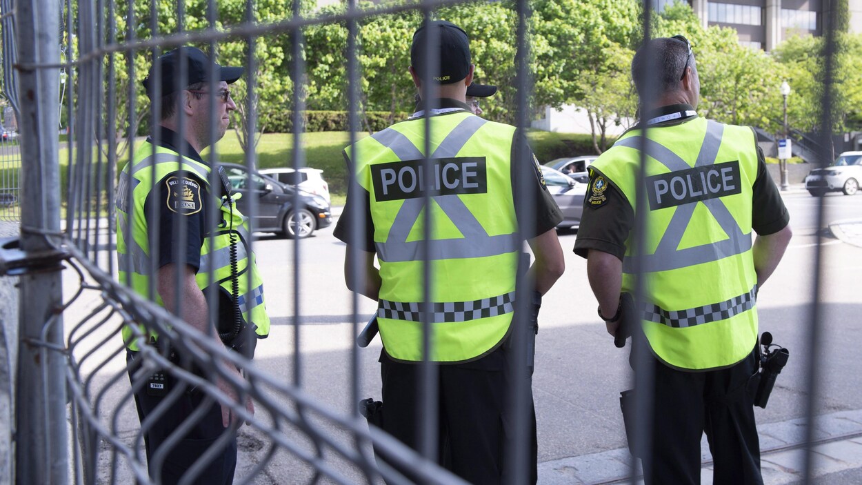 Trois policiers se tiennent devant une clôture grillagée.