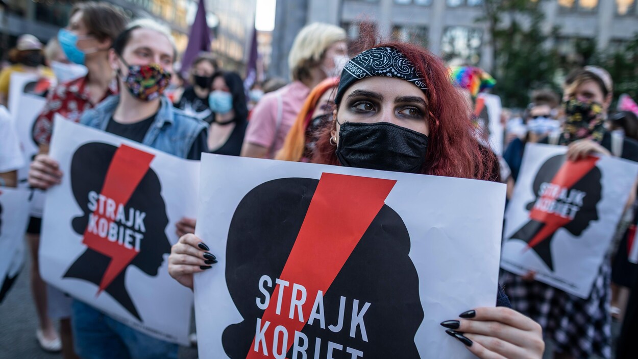 Des femmes masquées manifestent dans les rues de Varsovie avec des pancartes disant « grève des femmes » en polonais.
