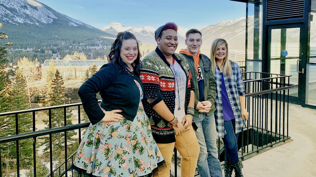 Quatre personnes se tiennent le long d'une barrière, devant des montagnes.