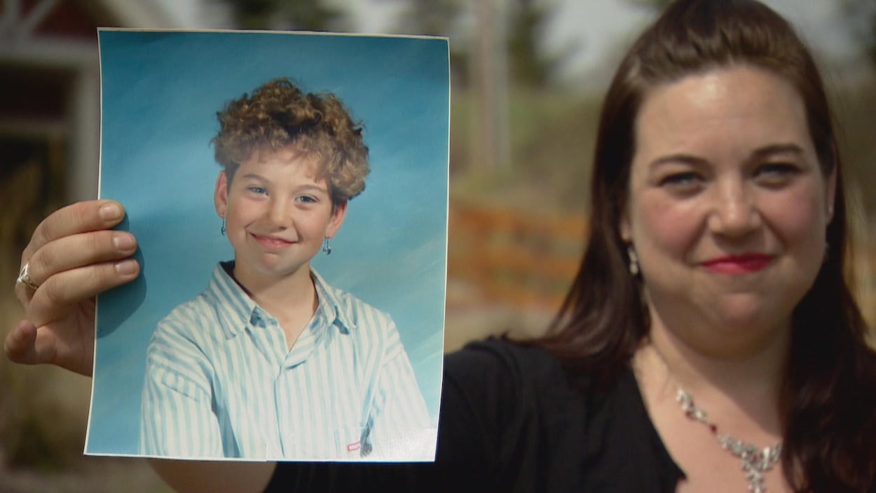 Une femme tient dans sa main droite une photo d'elle-même lorsqu'elle avait 10 ans.