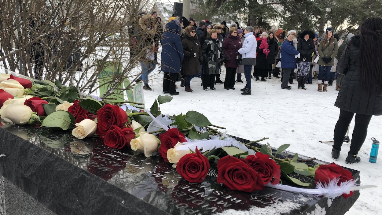 Des roses rouges et blanches déposées sur plaque commémorative et des personnes debout solennellement