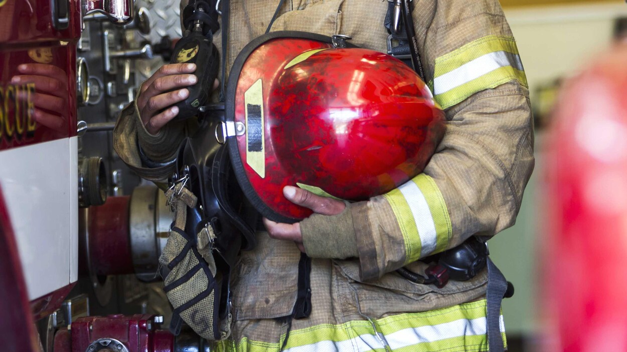 Un pompier couvert de suie tient un casque.