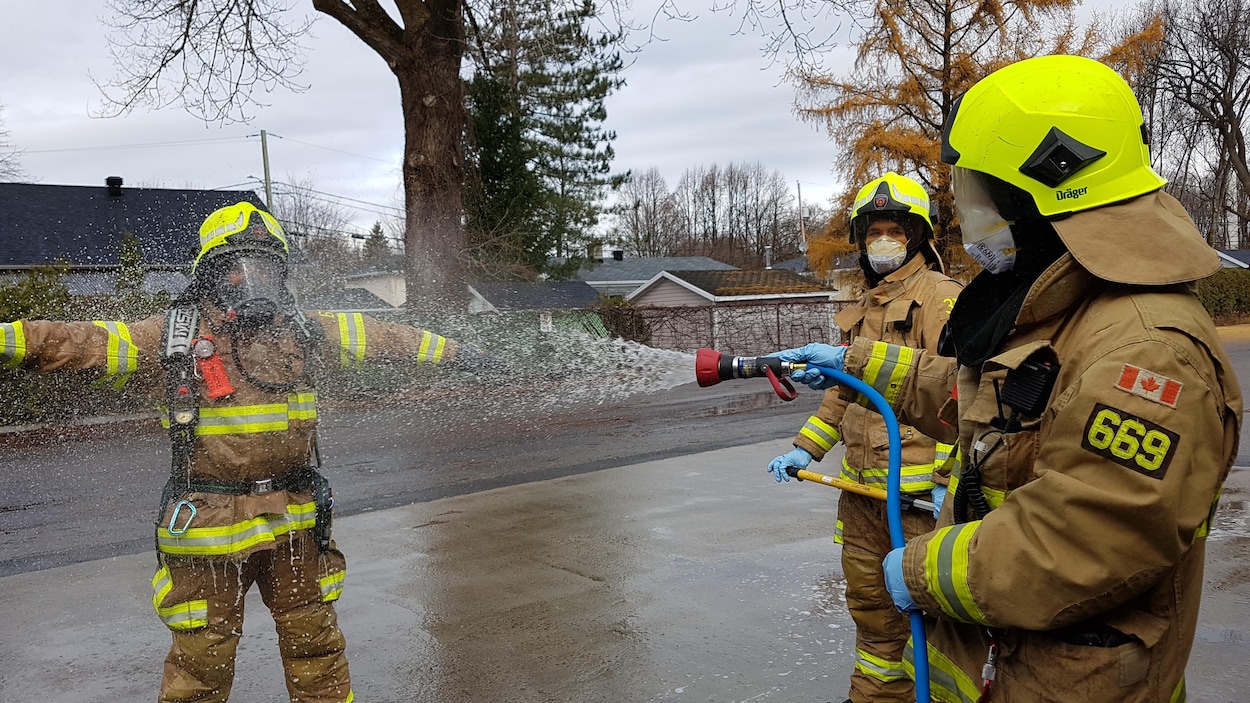 Un pompier rince l'équipement d'un collègue à l'aide d'un boyau d'arrosage sur les lieux d'un incendie.