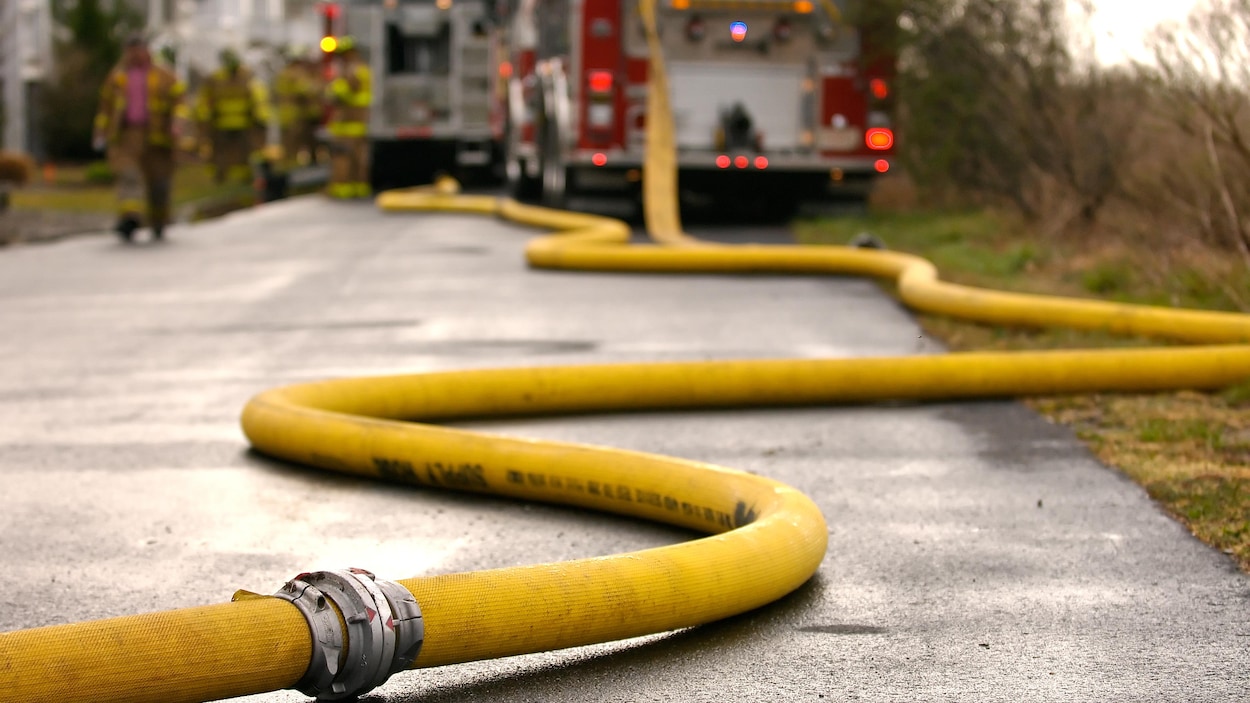 Boyau d'incendie sur le sol et pompiers en arrière-plan.
