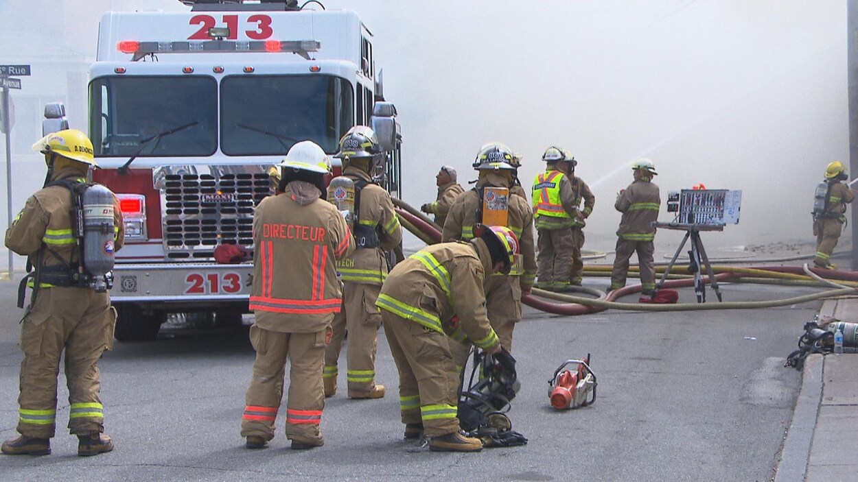 Des pompiers devant un camion de pompiers avec beaucoup de fumée