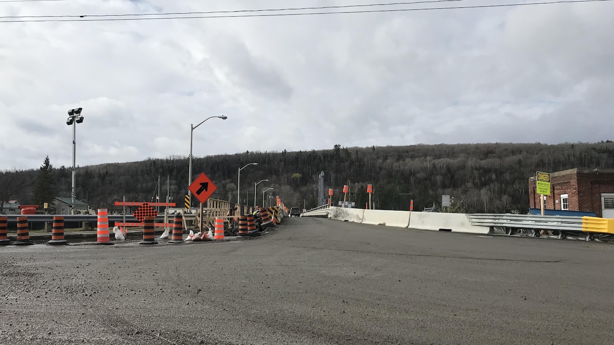 Route menant vers un pont en réfection avec de nombreux cônes et pancartes.