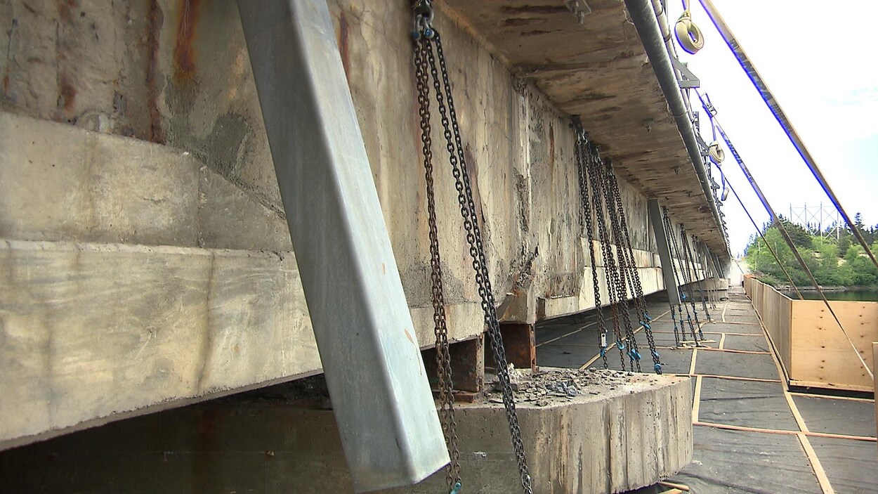 Des câbles relient le pont à une plateforme qui permet à des travailleurs de réparer le dessous du pont.