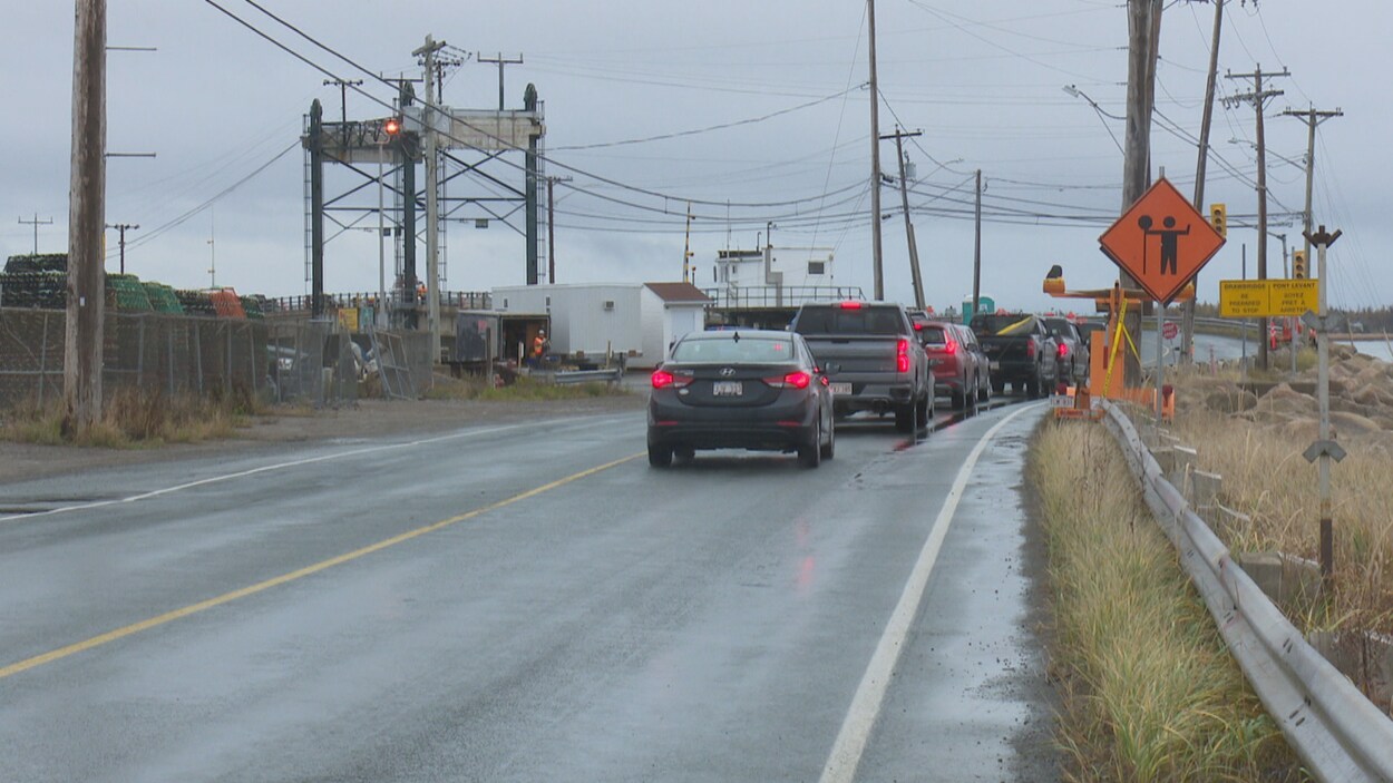 Le pont de Lamèque-Shippagan. La circulation se fait en alternance. Sur la route, six voitures attendent leur tour pour passer. Des affiches de constructions longent la voie.
