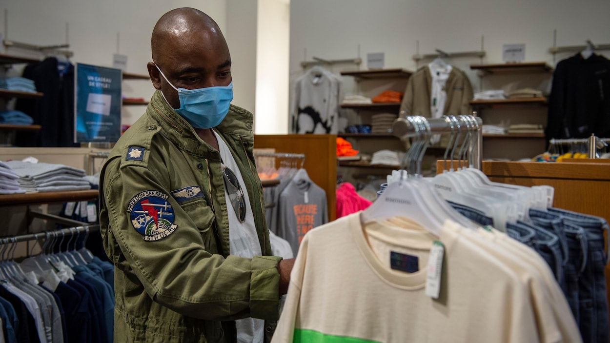 Un homme masqué regarde des vêtements dans un magasin.