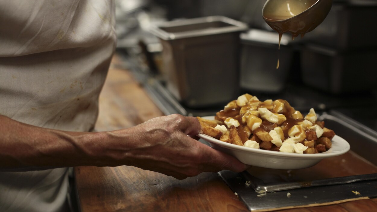 Un cuisinier ajoute de la sauce sur une poutine traditionnelle. Un cuisinier ajoute de la sauce sur une poutine traditionnelle.