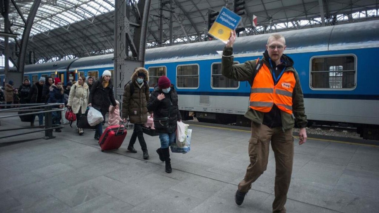 Un bénévole tenant une pancarte indique le chemin à suivre à des réfugiés ukrainiens.