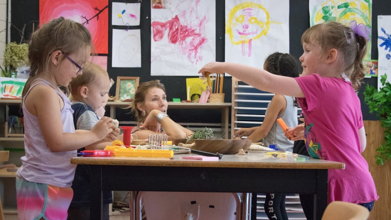 Des enfants jouent autour d'une table en compagnie d'une enseignante.