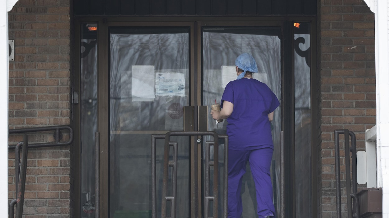 Une femme de dos en tenue de travail devant l'entrée du CHSLD.
