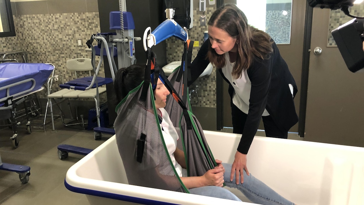 Une femme aide une autre femme à sortir d'une baignoire en utilisant un lève-personne.