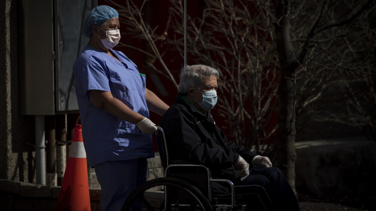 Une préposée avec un patient en fauteuil roulant, tous deux portant un masque.