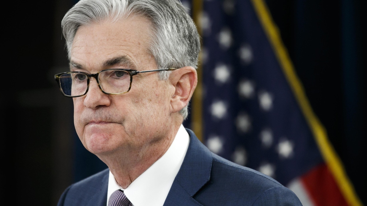 Jerome Powell l'air sérieux devant un drapeau américain.