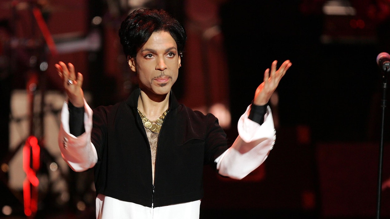 Le musicien Prince lève ses mains vers le ciel alors qu'il se tient sur scène lors d'un spectacle.