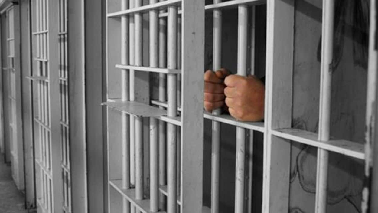 Des mains tiennent des barres dans une prison.