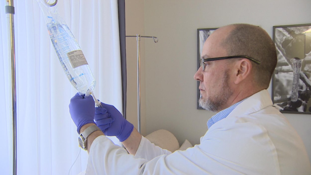 Un homme habillé d'un sarrau manipule une préparation médicamenteuse liquide.