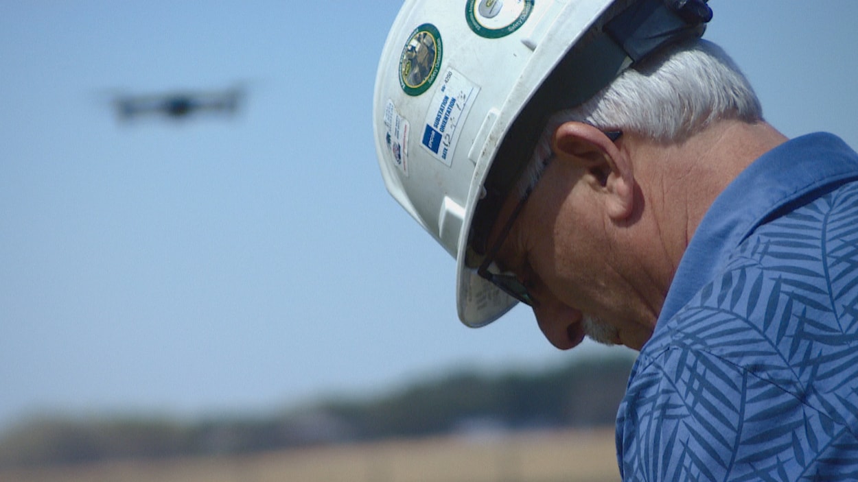 Tom Dudley, pilote professionnel, avec un casque sur la tête en train de piloter un drone dans un champ près d'Edmonton.