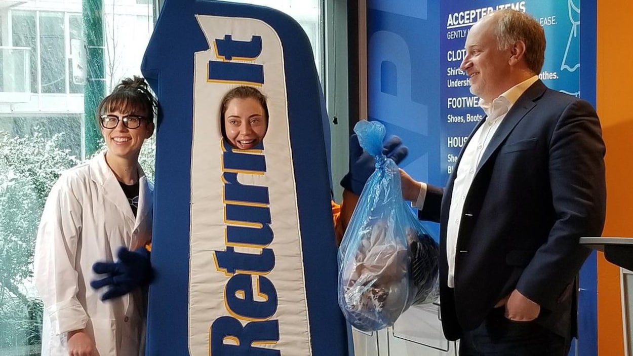 Une mascotte entourée de deux personnes reçoit un sac de vêtements usagés