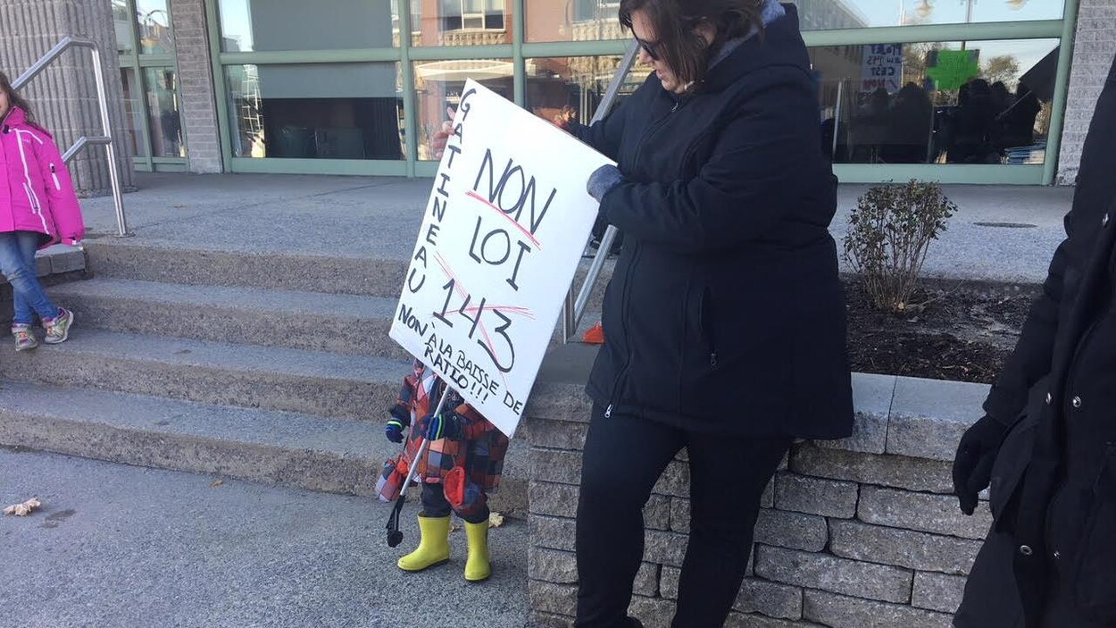 Une femme et un enfant tenant une pancarte dénonçant la loi 143 à Gatineau Une femme et un enfant tenant une pancarte dénonçant la loi 143 à Gatineau