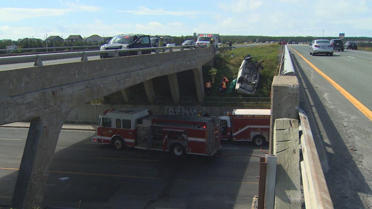 La scène de l'accident sur une autoroute montrant des camions de pompiers et une voiture renversée.