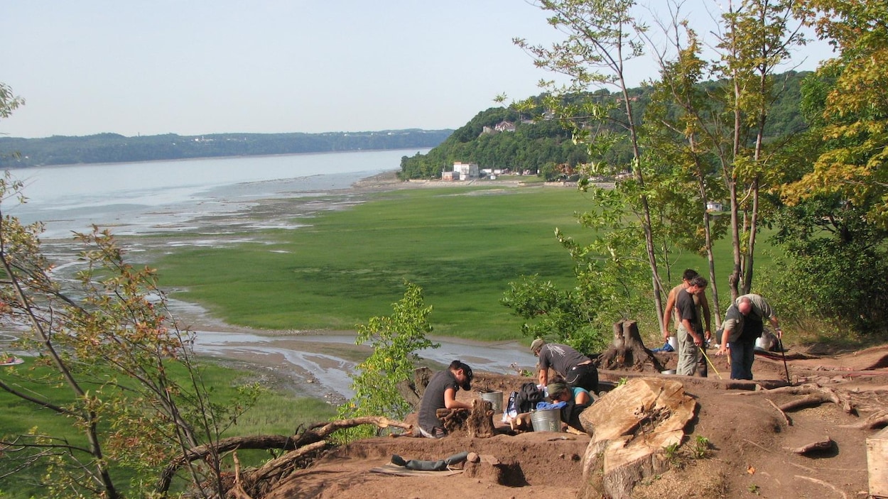 Des archéologues effectuent des fouilles sur le site Cartier-Roberval, au sommet du promontoire de Cap-Rouge. En contre-bas, on aperçoit le fleuve Saint-Laurent, l’embouchure de la rivière du Cap Rouge et la rive sud. La photographie a été prise en été.
