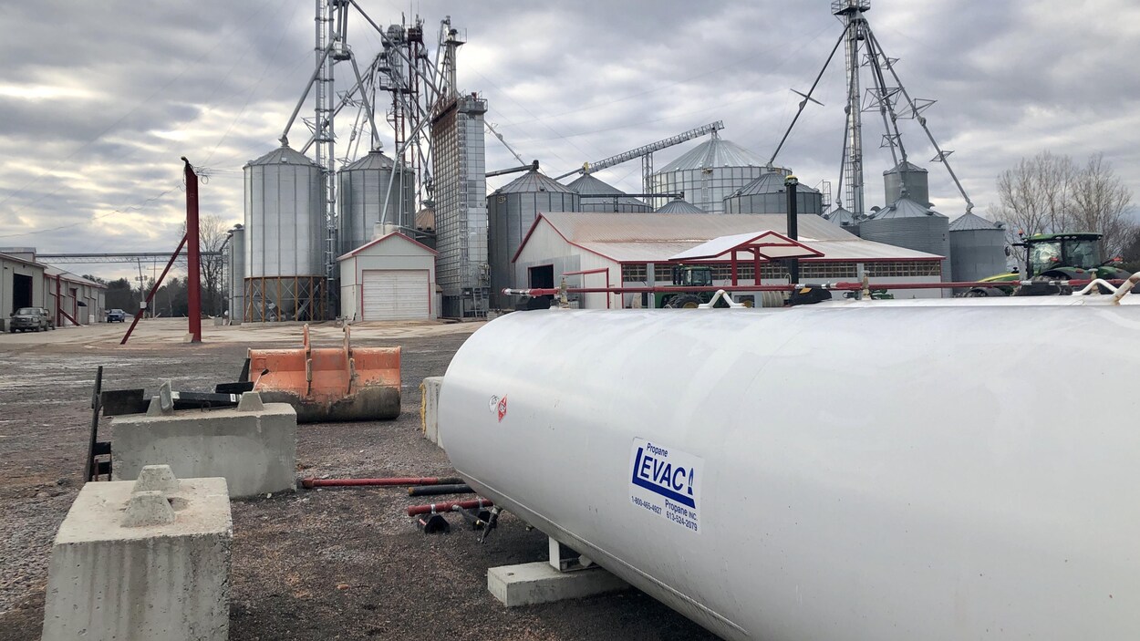 Une bobonne de propane près de silos et d'un séchoir à grain sur une ferme en automne.