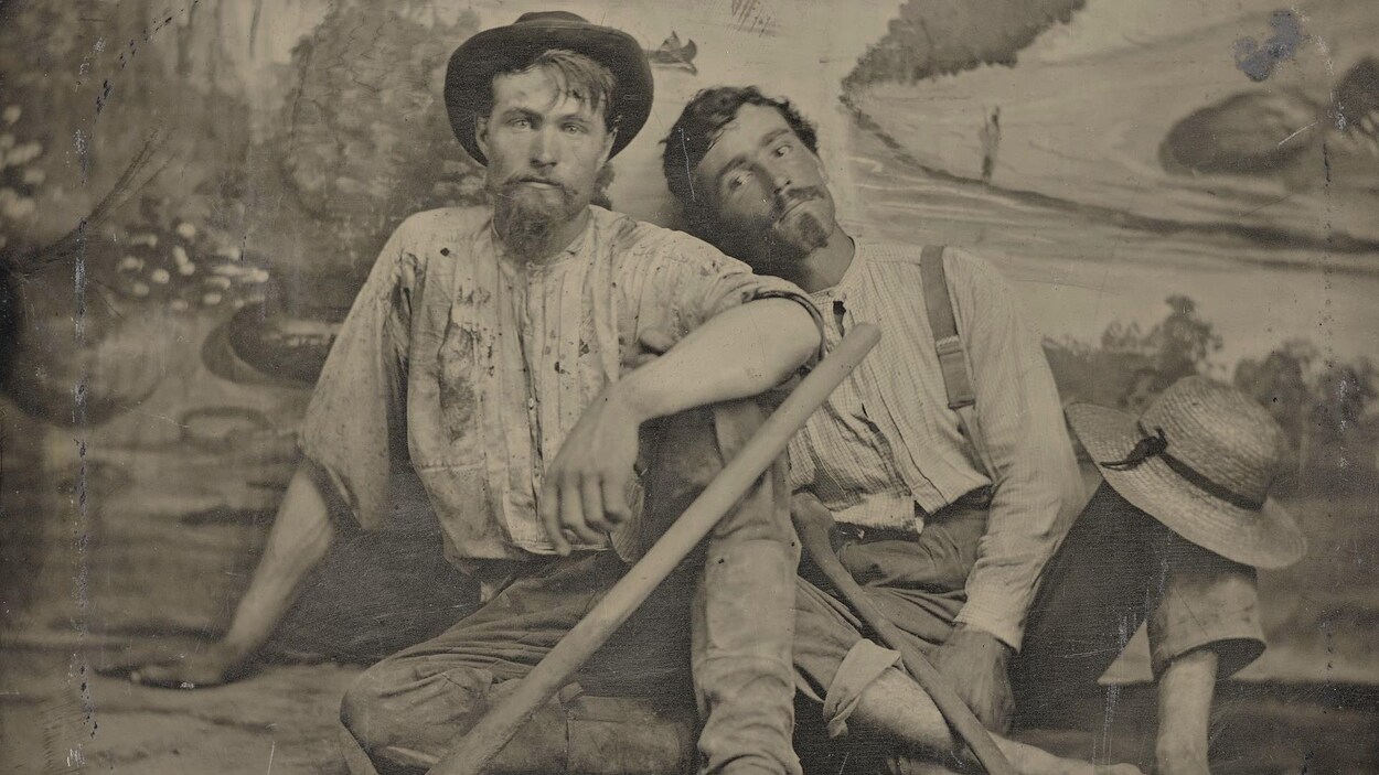 C'est une photo ancienne montrant les deux hommes assis par terre, dans leurs vêtements de prospecteurs, devant une tapisserie de studio de photo. Ils ont l'air sales et plutôt fatigués.