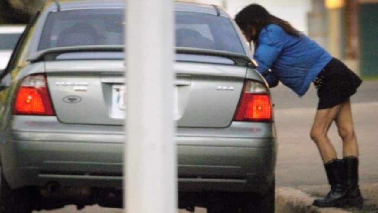 Une femme sur un trottoir parle à un automobiliste assis dans sa voiture.