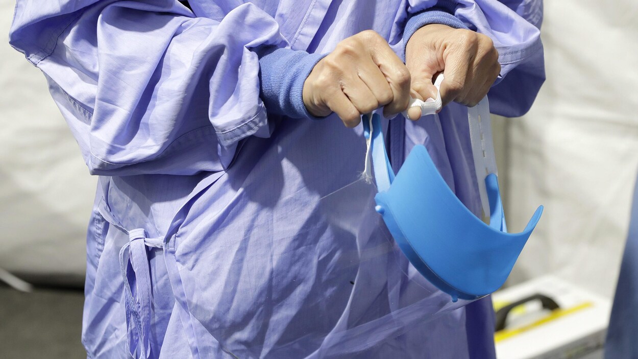 Une infirmière vêtue d'une jaquette médicale bleue ajuste une visière.