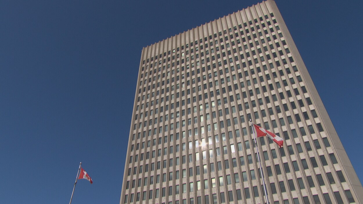Deux drapeaux du Canada flottent devant une tour à bureaux du gouvernement fédéral à Ottawa.