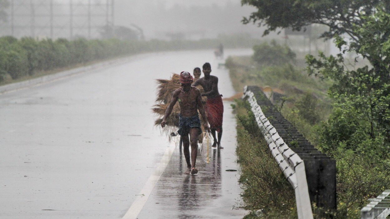 Trois hommes marchent le long d'une route sous la pluie en transportant quelques biens.