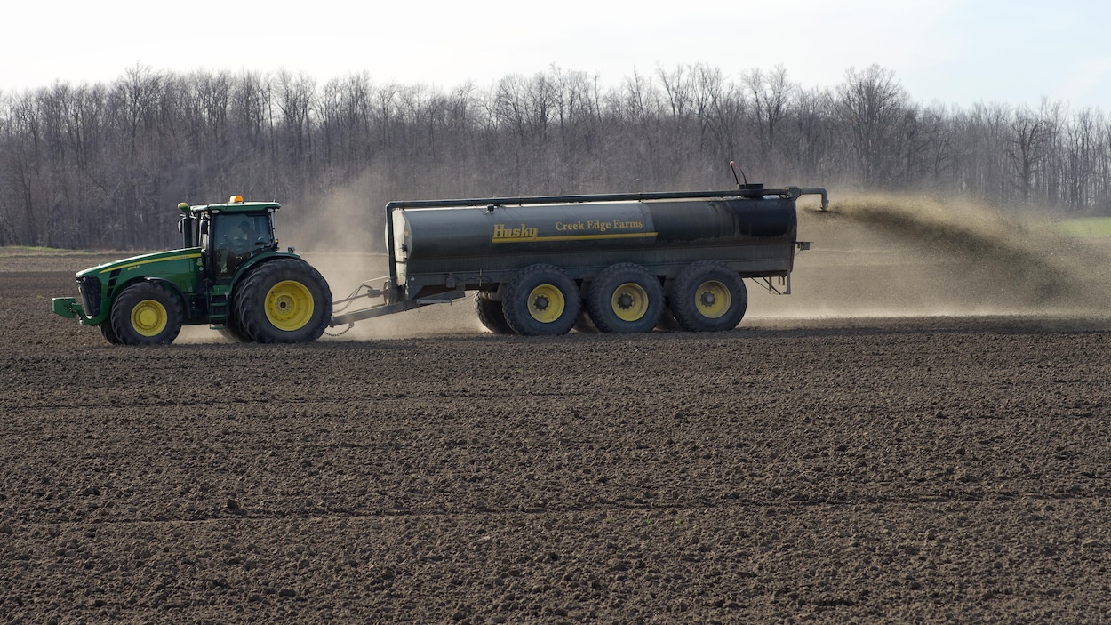 Un imposant tracteur John Deere déversant du lisier dans un champ.