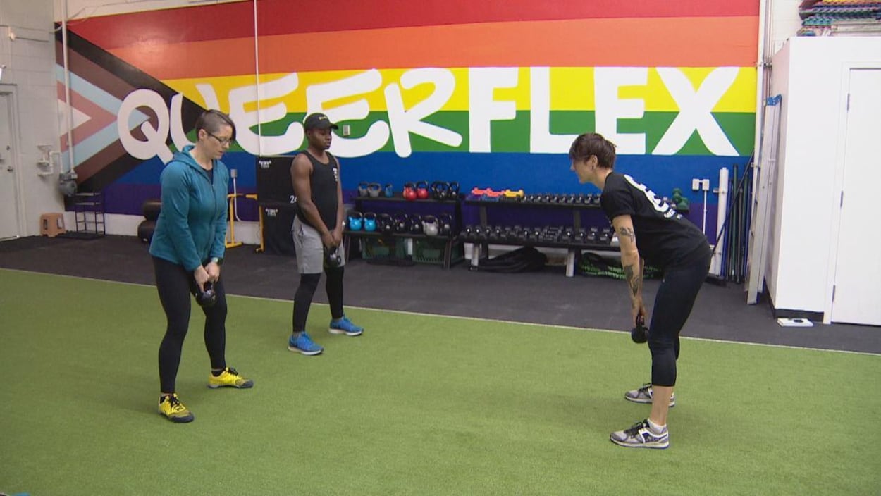 Trois personnes s'entraînent avec des poids sur un tapis imitant de l'herbe, devant un mur arborant le drapeau arc-en-ciel sur lequel est écrit Queerflex, le nom du gym.