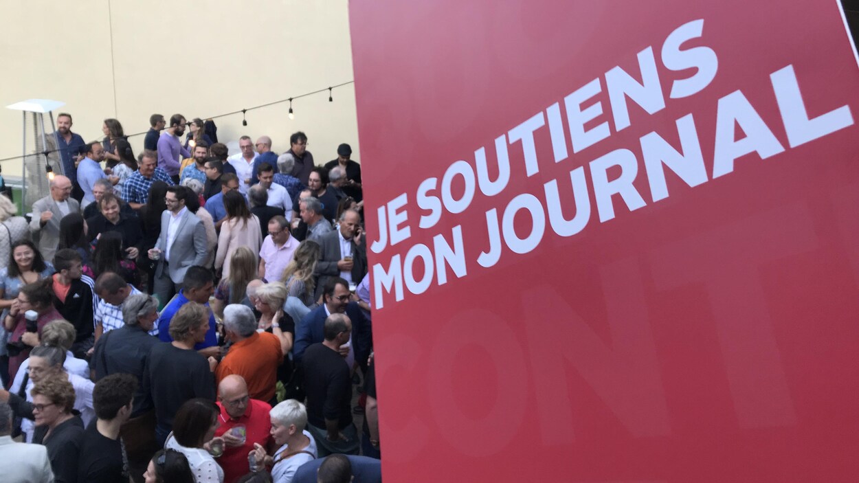 Une pancarte sur laquelle on peut lire "Je soutiens mon journal" et des gens sur une terrasse.