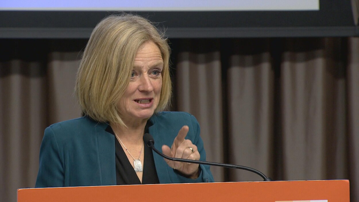 Plan moyen de Rachel Notley derrière un lutrin surmonté d'un micro.