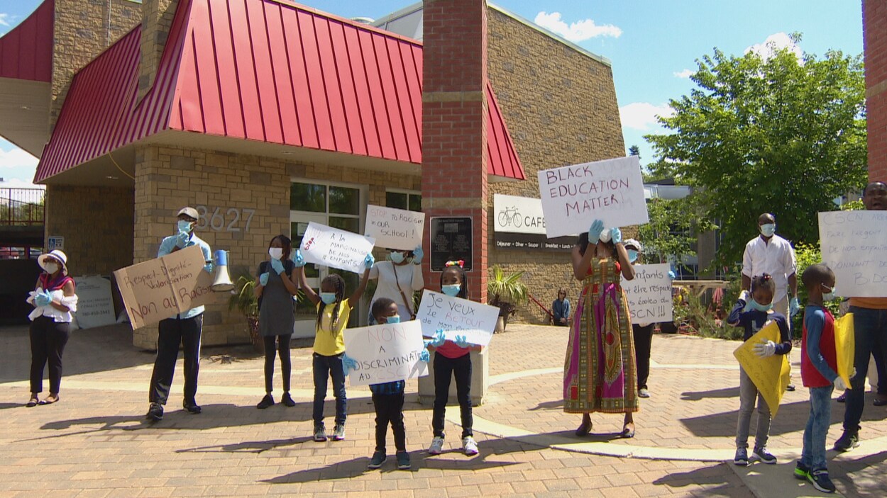Un groupe de personnes Noires tiennent des pancartes devant un édifice.